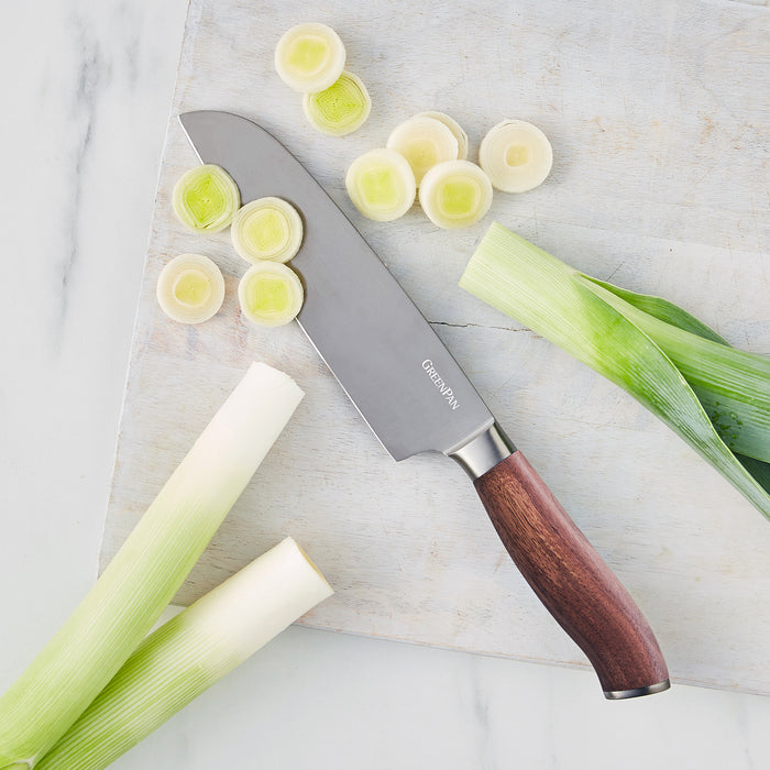 Santoku knife with walnut handle slicing leeks on a wooden cutting board.