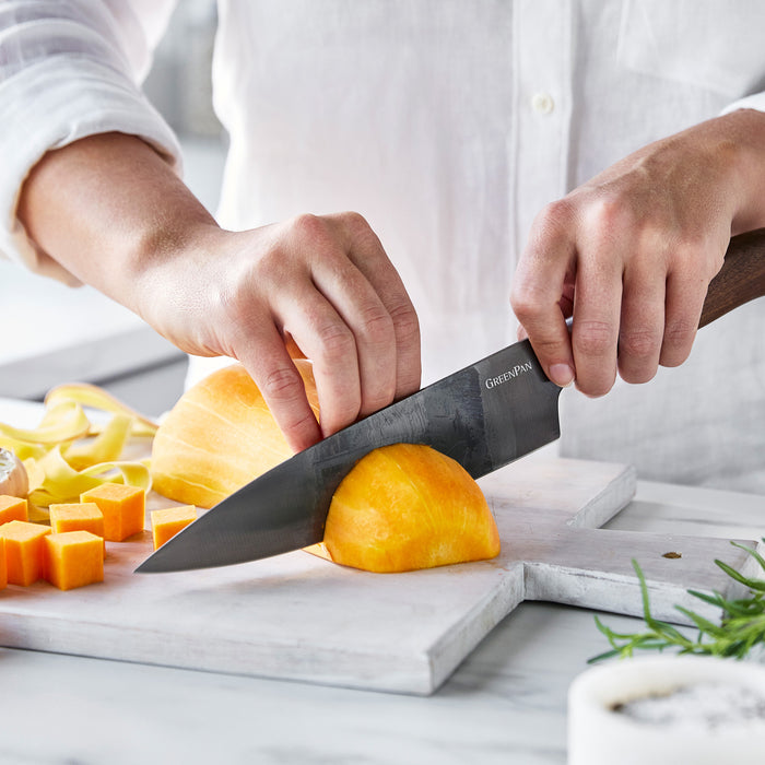 Yellow squash being sliced on a white cutting board with a Premiere Titanium Cutlery 8 chefs knife; diced pieces nearby.