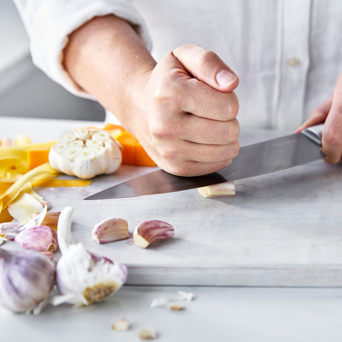 Chefs knife with walnut handle crushing garlic cloves on a wooden cutting board.