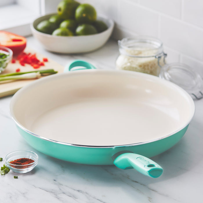 Turquoise ceramic 13.5-inch frypan with stay-cool handle on a counter surrounded by cooking ingredients.