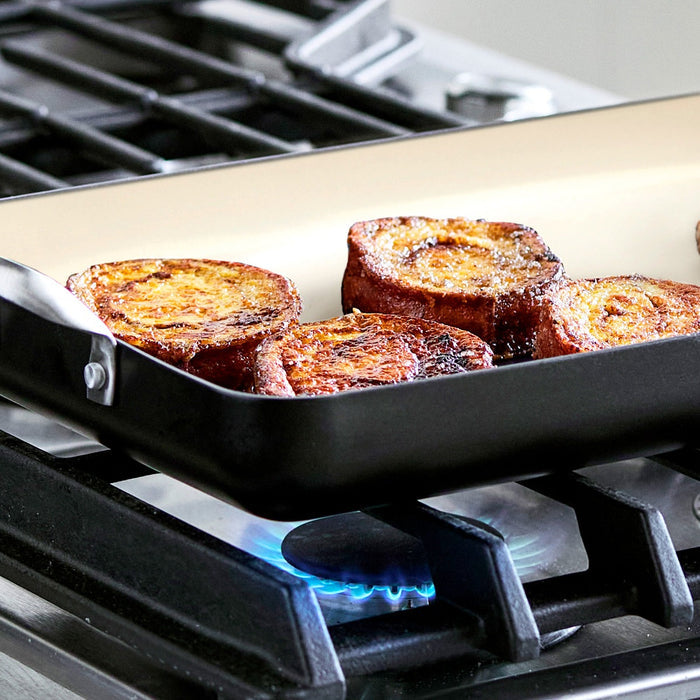 French toast on black Rio Double Griddle with stainless handles over blue gas flame.