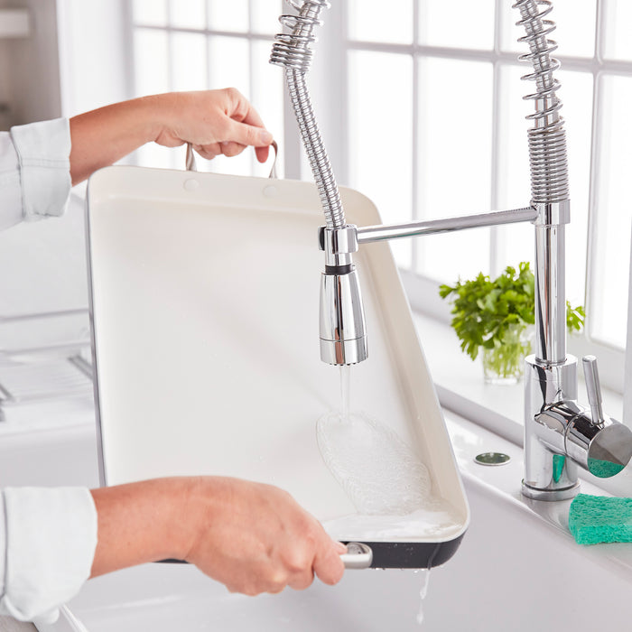 Person rinsing a black Rio Double Griddle under a modern kitchen faucet in a well-lit kitchen.