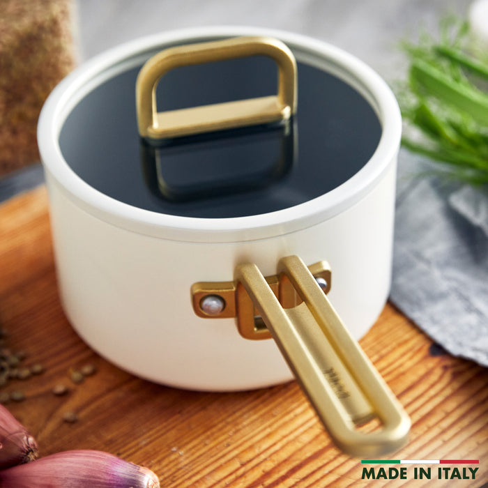 White ceramic saucepan with lid on wood, surrounded by fresh herbs, onions, and spices. 2-quart size.