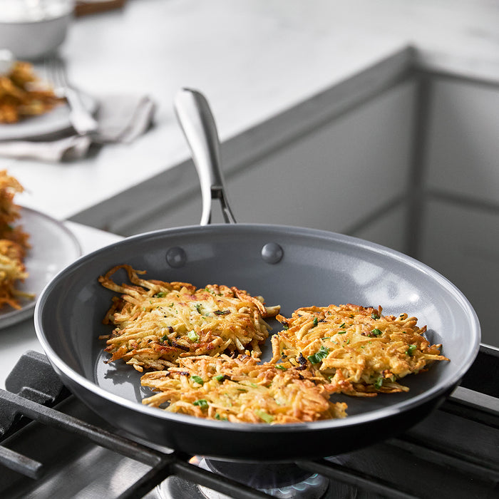 Three latkes frying in a gold Swift 10 ceramic frypan on a stovetop in a modern kitchen.