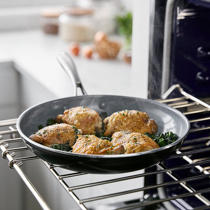 Ceramic nonstick 10-inch frypan with baked chicken thighs and herb garnish on an open oven rack.