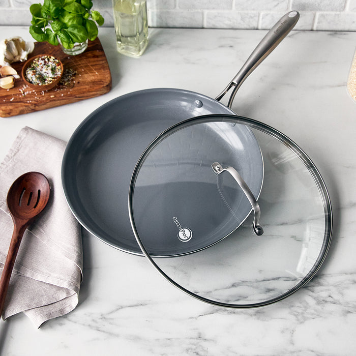 Ceramic nonstick 12-inch frypan with lid and stainless steel handle on a marble countertop.