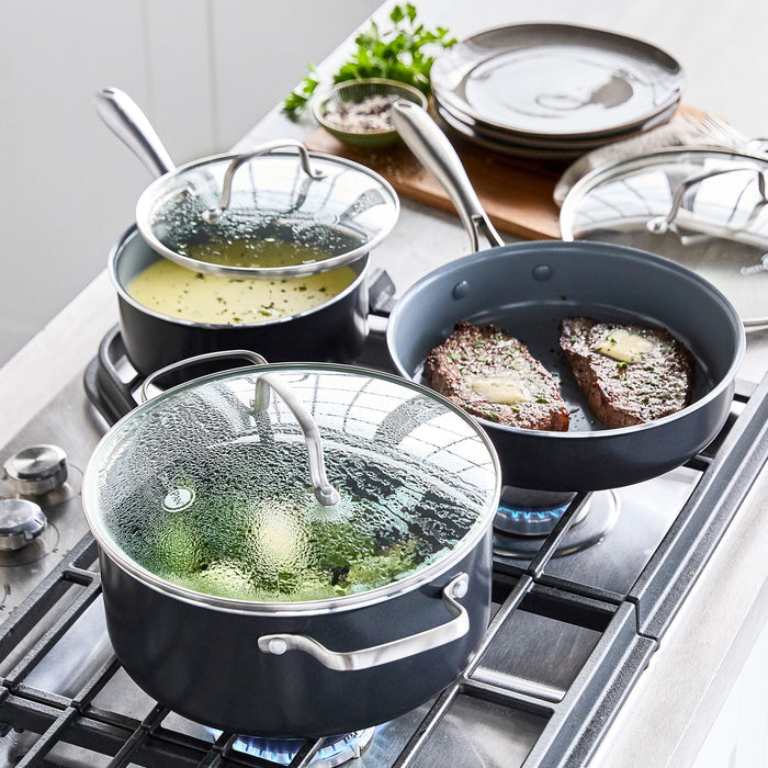 Ceramic nonstick 17-piece cookware set in assorted sizes and colors displayed on a stovetop with food inside pans.