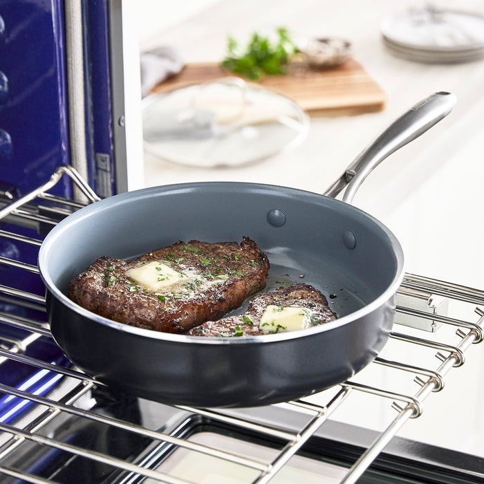 Two steaks with melting butter in a ceramic nonstick skillet, kitchen background softly blurred.