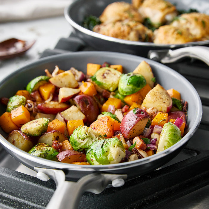 Brussels sprouts, potatoes, and squash in two grey Swift ceramic nonstick frypans, 8-inch and 10-inch sizes.