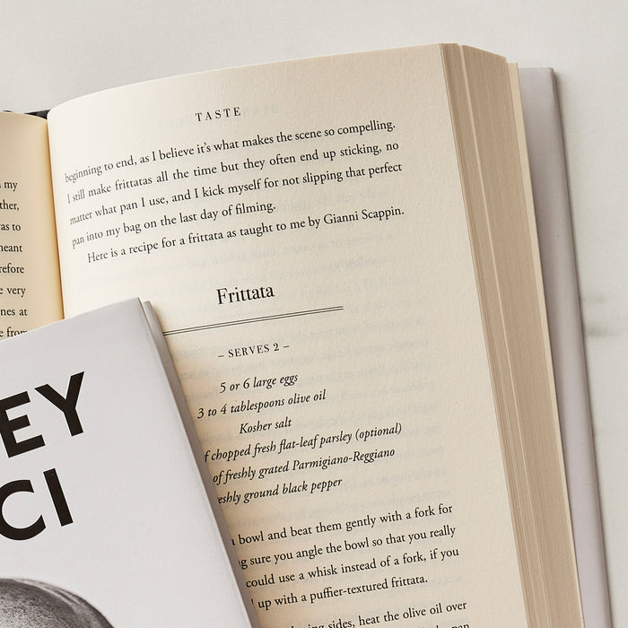 Taste: My Life Through Food cookbook open on a surface, partially covered, pages featuring a recipe and food photography.