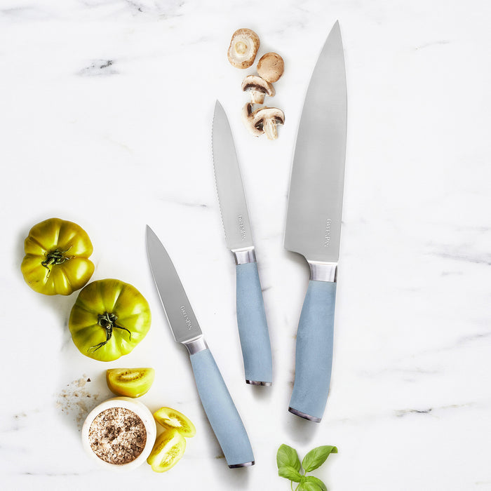 Three-piece blue titanium knife set on marble, displayed with green tomatoes, mushrooms, basil, and salt.