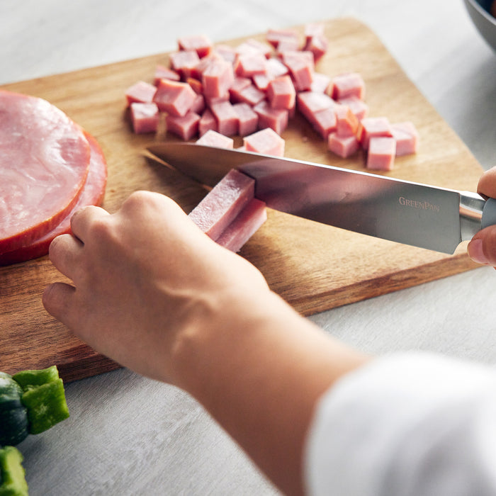 Person cubing ham on a wooden board using a blue-hued Titanium Cutlery 3-piece knife set.