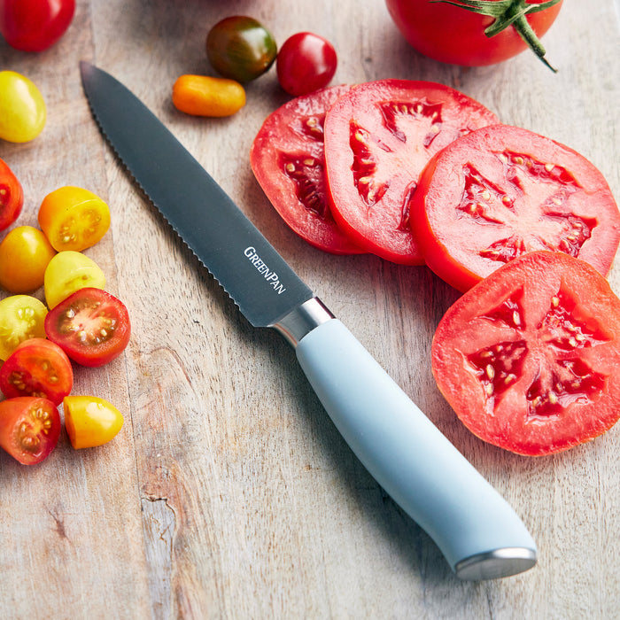 Three blue titanium knives beside sliced and whole tomatoes on a wooden board.