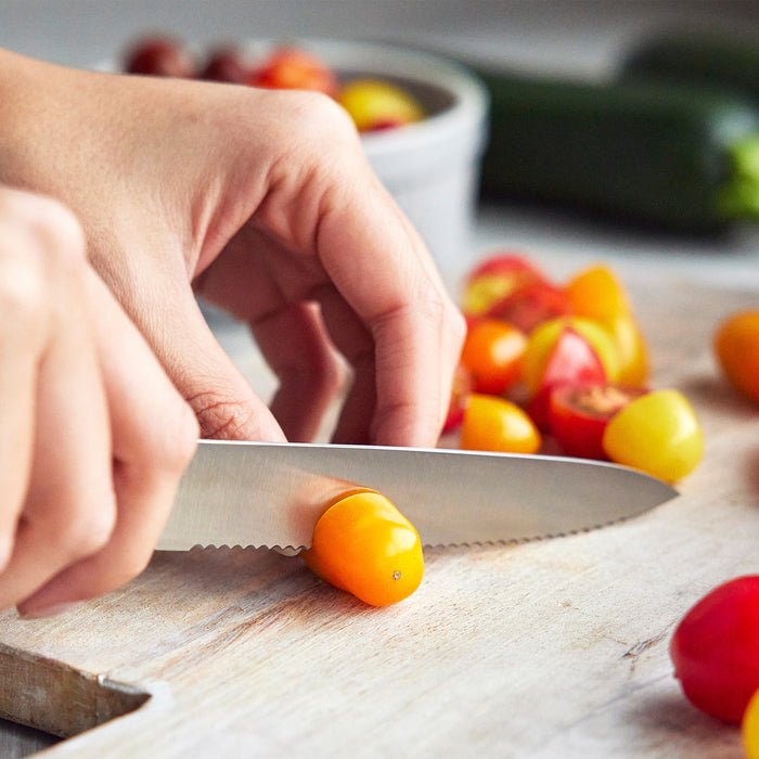 Slicing a yellow cherry tomato with a Blue Haze titanium knife; two more knives from the set rest on the cutting board.