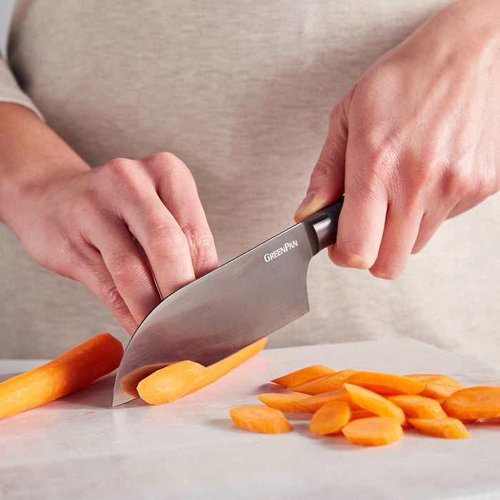Titanium Cutlery 5″ Santoku knife slicing a carrot on a white cutting board, with thin carrot rounds and a stick visible.