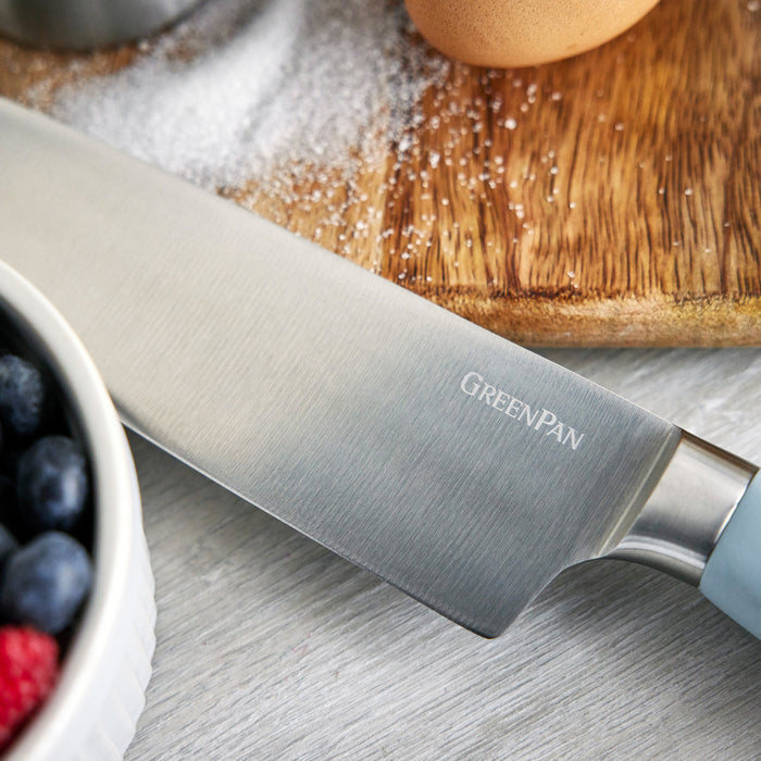 Blue Haze titanium chefs knife from 16-piece set shown near berries, egg, and spilled salt on a countertop.