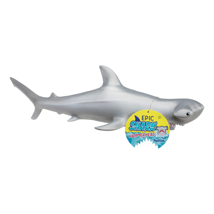 The Toysmith Epic Shark - Hammerhead is a soft gray plastic toy with cartoonish details, a smooth texture, and an “Epic Shark Hammerhead” tag in its mouth, making it a fun educational toy for kids.