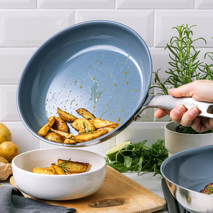 Roasted potato wedges being poured from a ceramic nonstick pan into a white bowl with herbs.