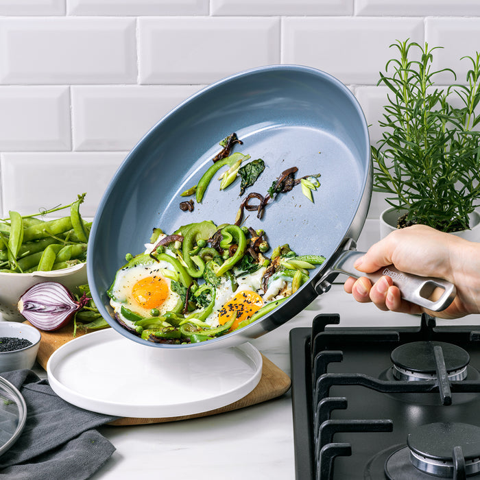Hand pouring eggs and vegetables from a stainless steel nonstick frypan onto a plate by the stove.