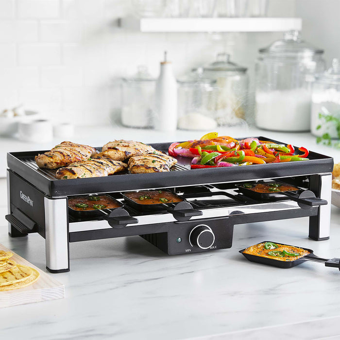 Electric grill on a white countertop cooking chicken, vegetables, and cheese in separate trays.