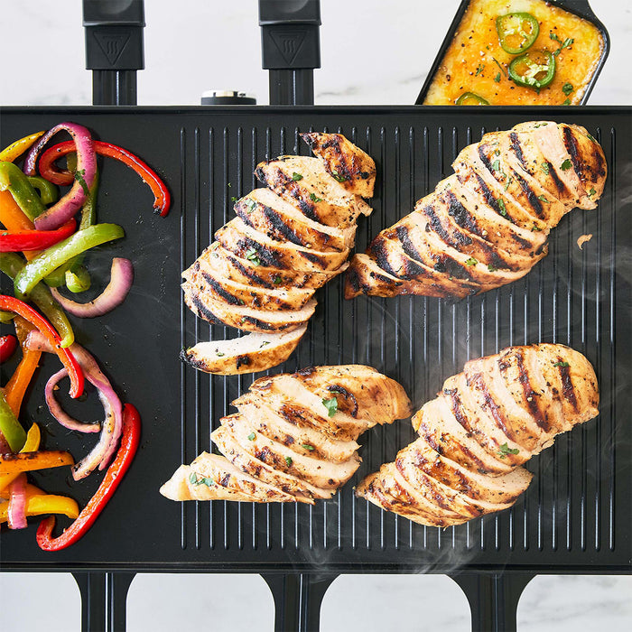 Grilled chicken slices with sautéed peppers and onions on a grill, cheesy casserole in a baking dish beside them.