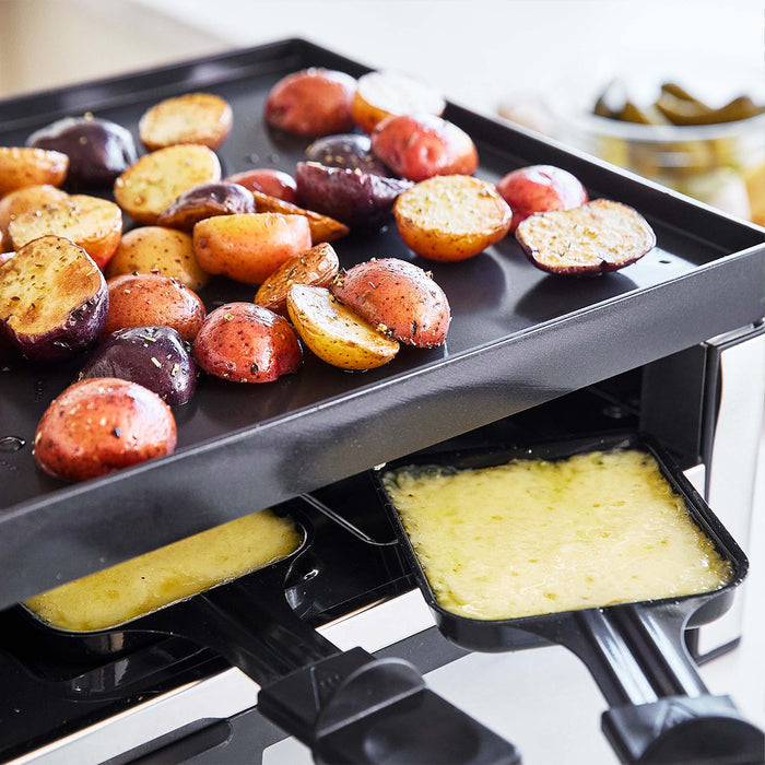 Halved roasted potatoes with melted cheese and pickles on the side, served on a black grill pan.