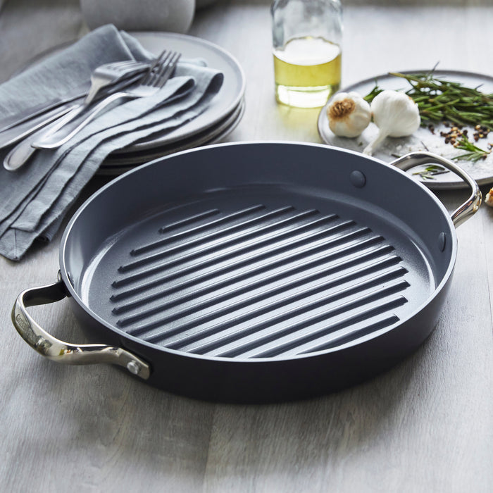 Round ceramic nonstick grill pan with metal handles on a table.