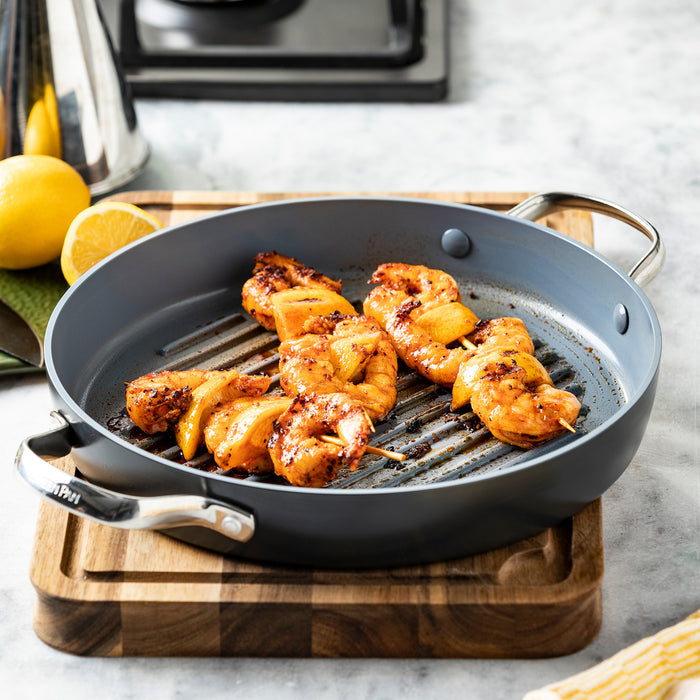 Grilled shrimp and lemon slices on a round ceramic nonstick grill pan with a wooden board underneath.