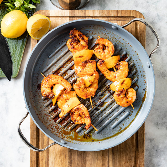Shrimp skewers and vegetables on a Valencia Pro ceramic nonstick grill pan, with lemon slices on the side.