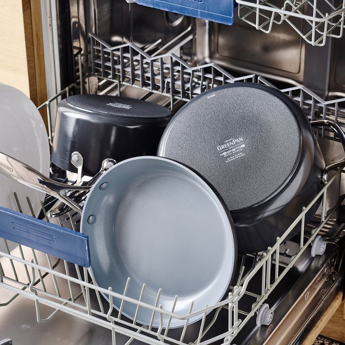 Open dishwasher with clean cookware, including a grey ceramic nonstick round grill pan among pots and pans.
