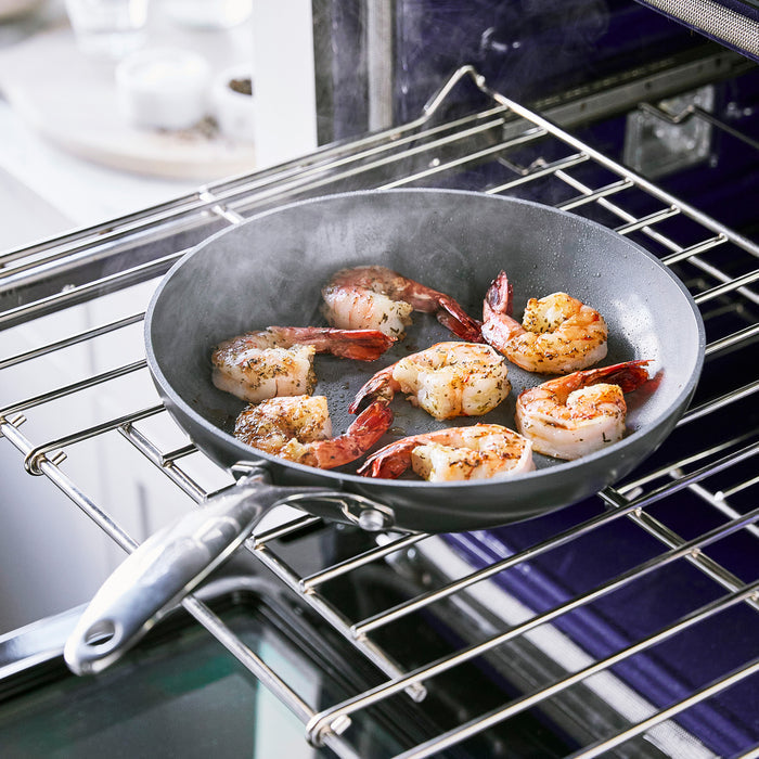 Shrimp cooking in a ceramic nonstick 12-inch frypan inside an open oven, steam visible above the pan.