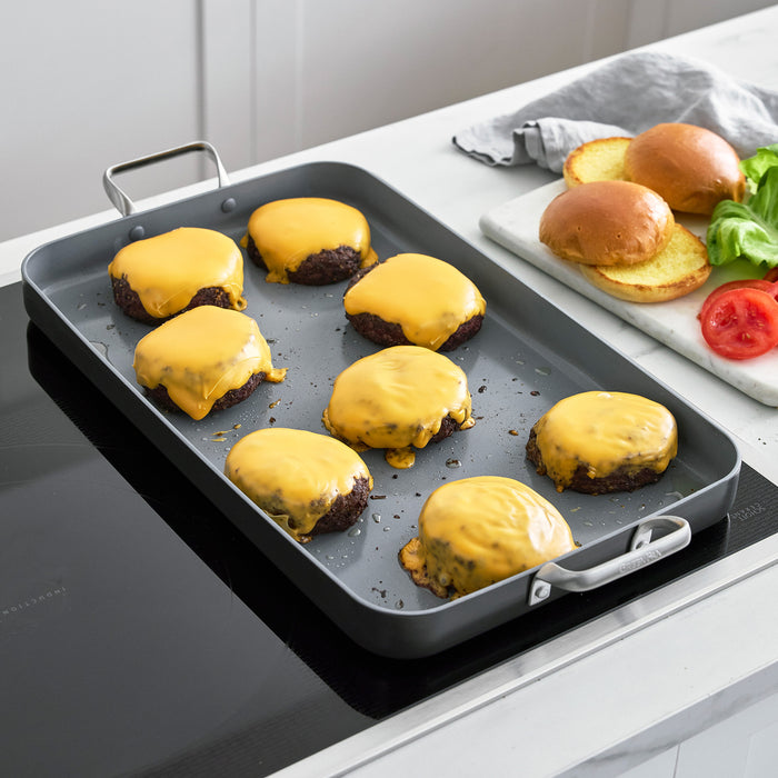Eight cheeseburgers with melted cheese cooking on a large rectangular ceramic nonstick griddle on a stovetop.