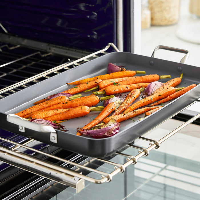 Chopped carrots and red onions on a gray ceramic nonstick griddle, ready for oven roasting.