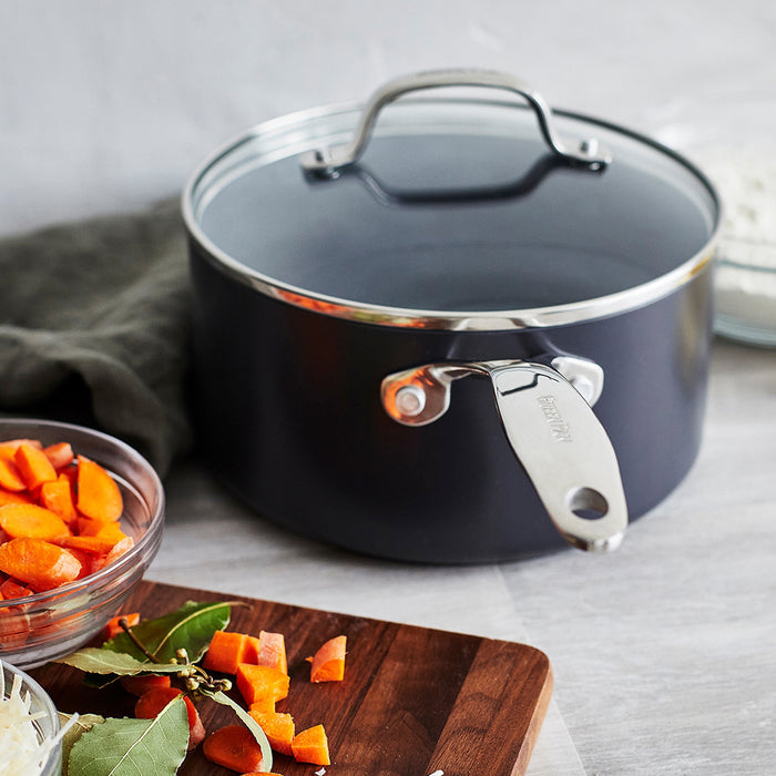 Gray saucepan on a kitchen counter with carrots and a cutting board