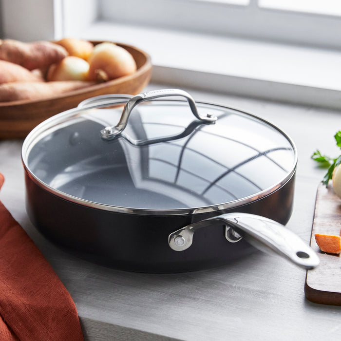 Gray ceramic nonstick sauté pan with lid on a countertop next to whole onions and sweet potatoes.