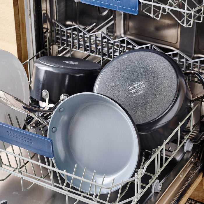 Open dishwasher with several pots and pans inside, including a grey ceramic sauté pan with glass lid.