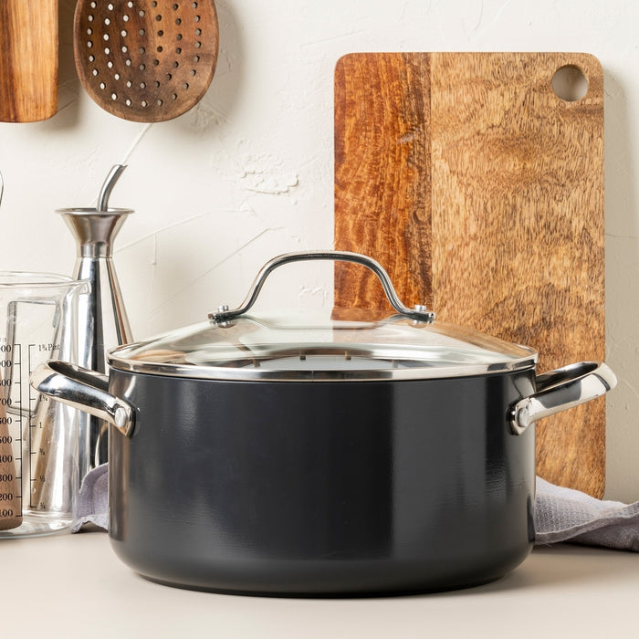 The Valencia Pro Ceramic Nonstick 5.5-Quart Stockpot with Lid rests on a kitchen counter in front of a wooden cutting board, surrounded by utensils and a glass measuring cup.
