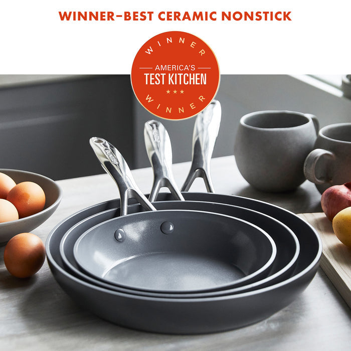 The Valencia Pro Ceramic Nonstick 8", 9.5", and 11" Frypan Set in gray is stacked on a kitchen counter with eggs, potatoes, and bowls nearby. A badge reads: Winner—Best Ceramic Nonstick, Americas Test Kitchen Winner.