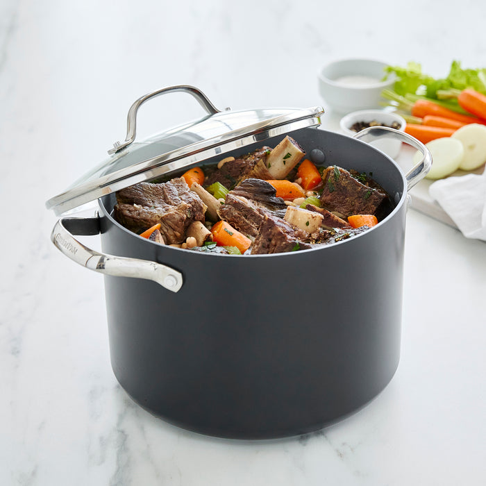 Gray ceramic stockpot with lid, filled with beef stew and vegetables, on a marble countertop.